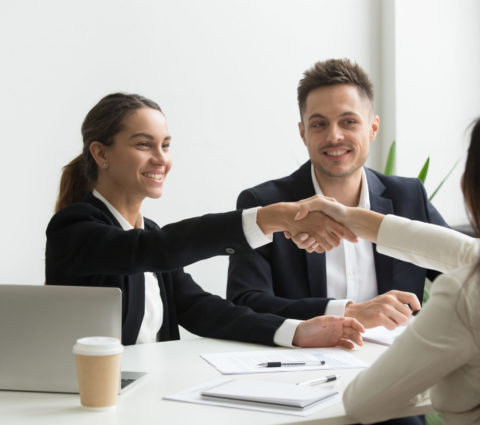 Smiling HR managers greeting female job applicant with handshake during recruiting or interview. Businesswoman making good first impression shaking hands of business partners. Partnership, cooperation