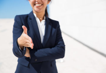 Smiling HR manager congratulating with getting job. Cropped portrait of positive woman in formal suit standing outdoors and offering hand for handshake. Business offer concept